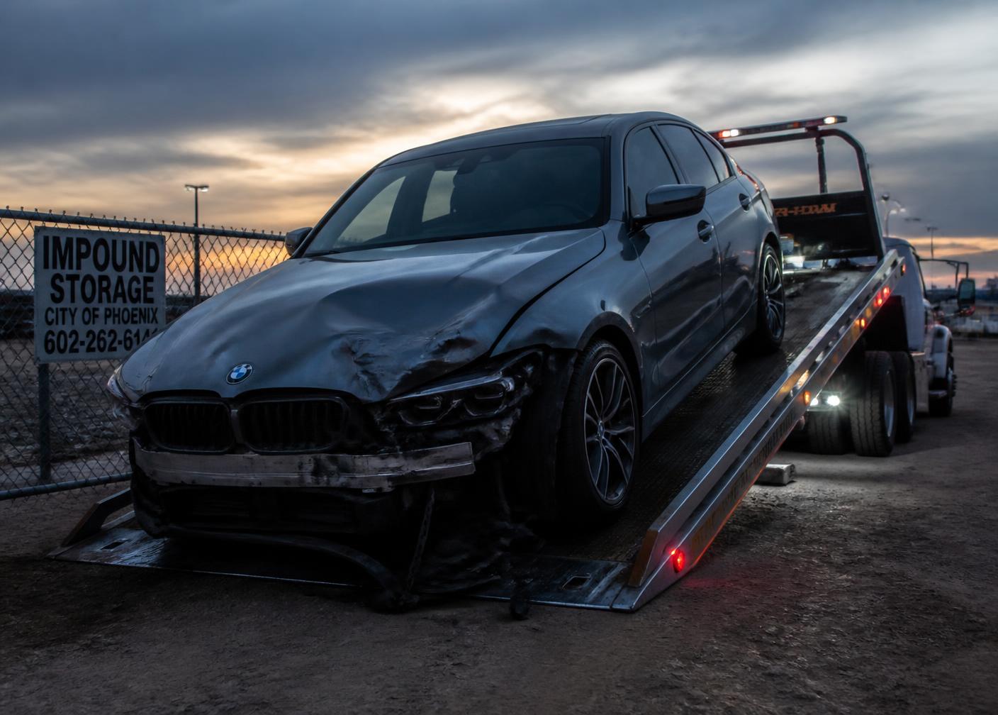 Damaged car being loaded onto a flatbed tow truck at an impound storage lot in Phoenix